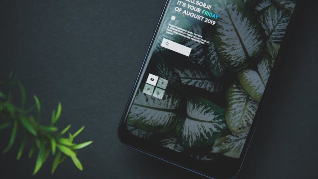 Close-up of a smartphone with a plant leaf wallpaper and apps displayed on the screen.