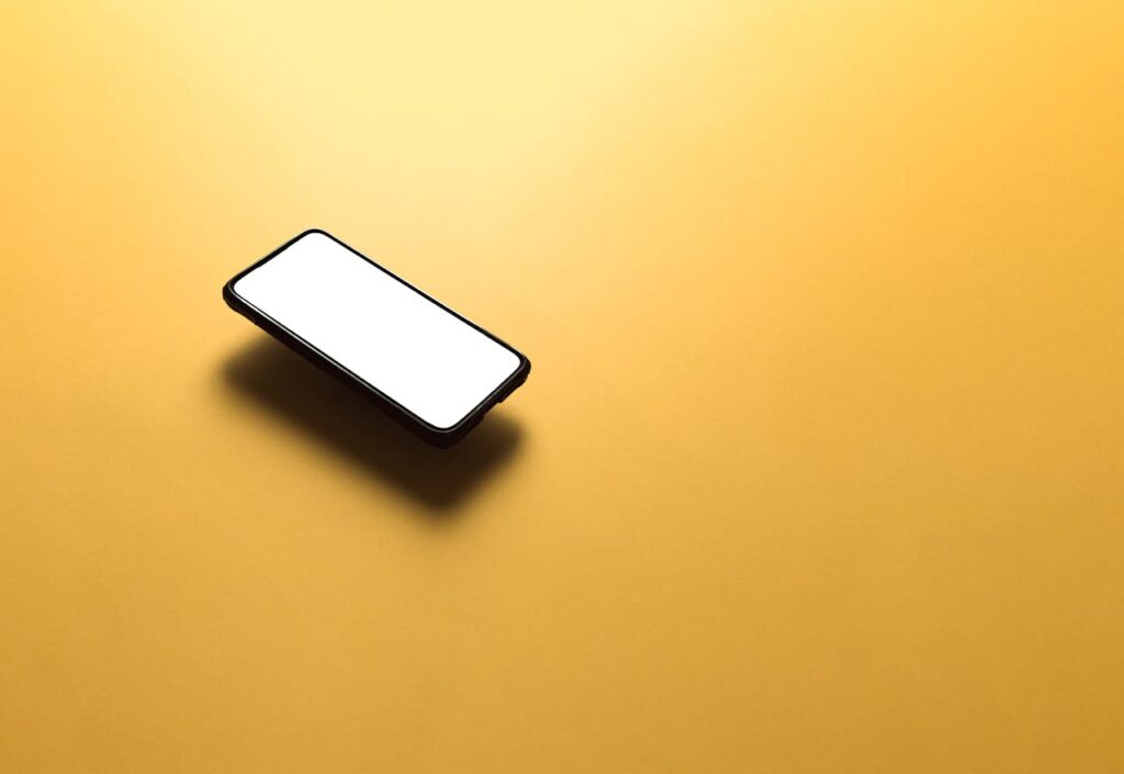 Smartphone with a blank white screen on a vibrant yellow surface, offering ample copyspace.